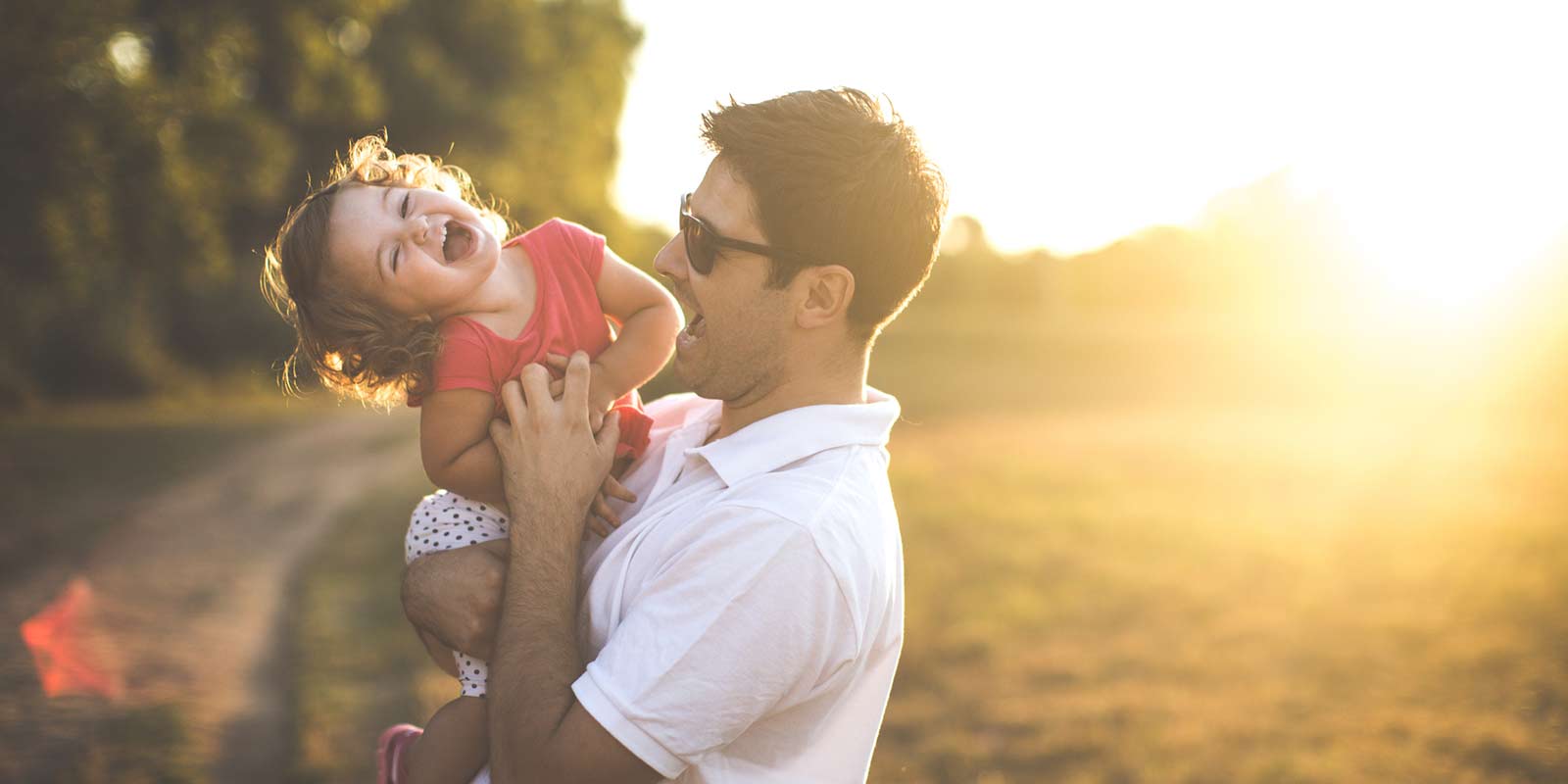 A little girl laughs as her father tickles her tummy in the sunset.