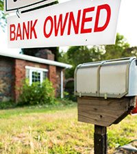 A home with a "Bank Owned" sign hanging on the mailbox. 