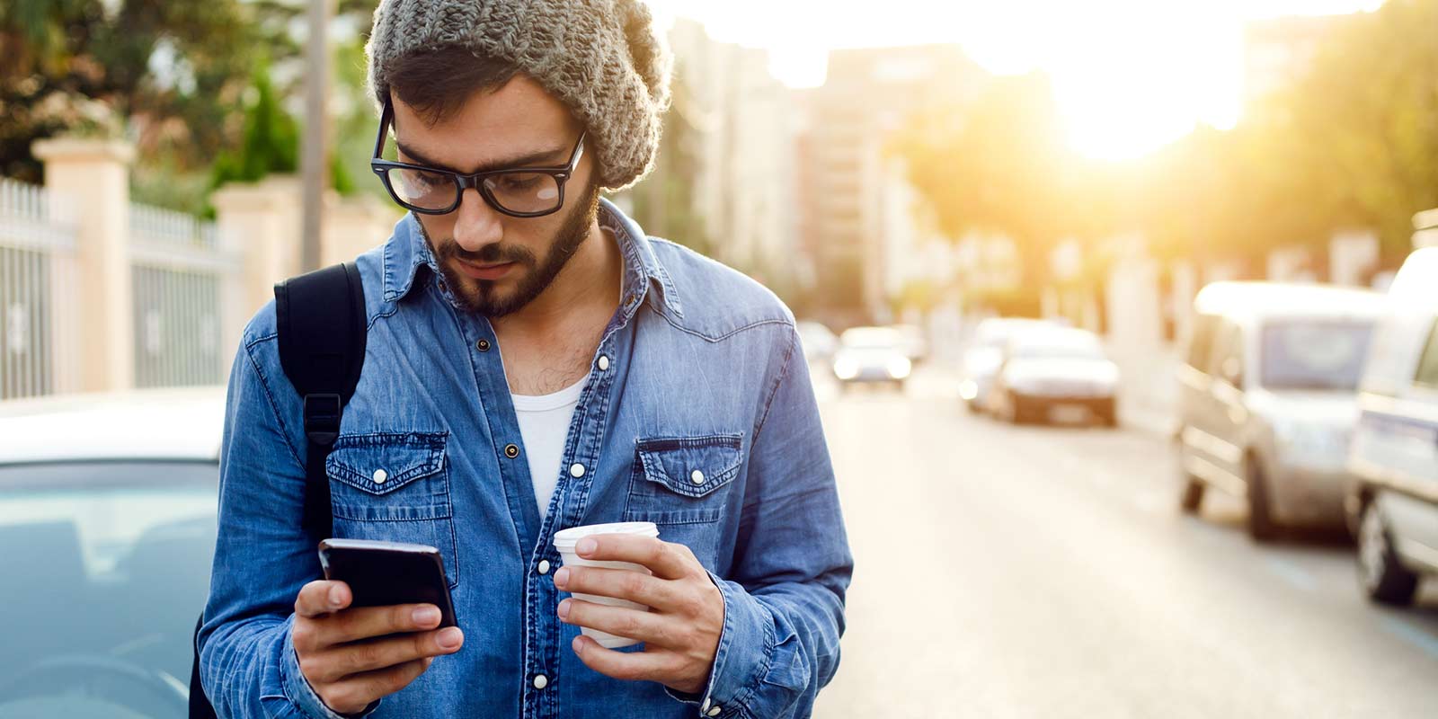 A man standing in the street looks down at his cellphone.