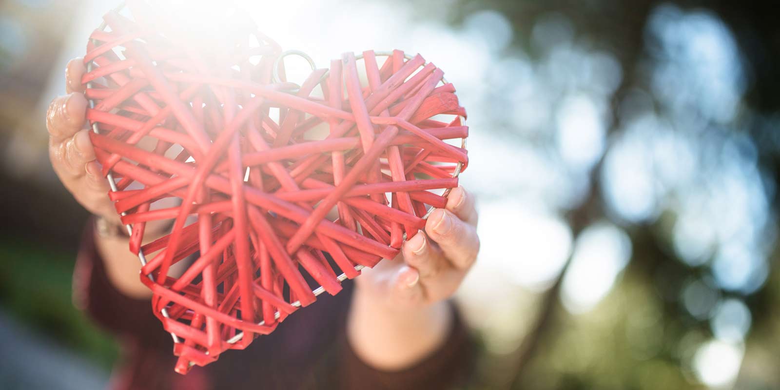 Hands reaching out and holding a heart constructed out of yarn.