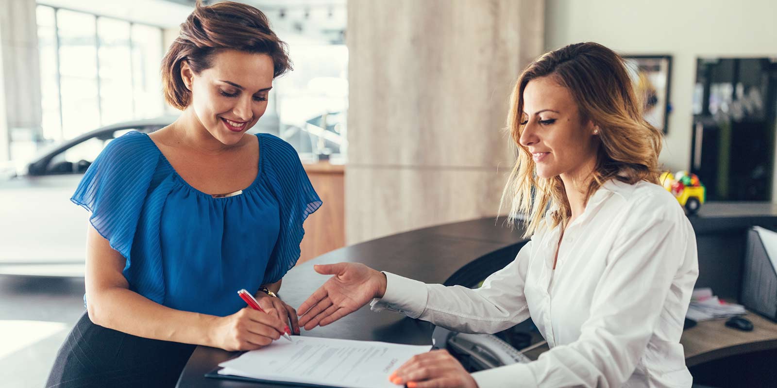 A woman stands and fills out a form at a car dealership.