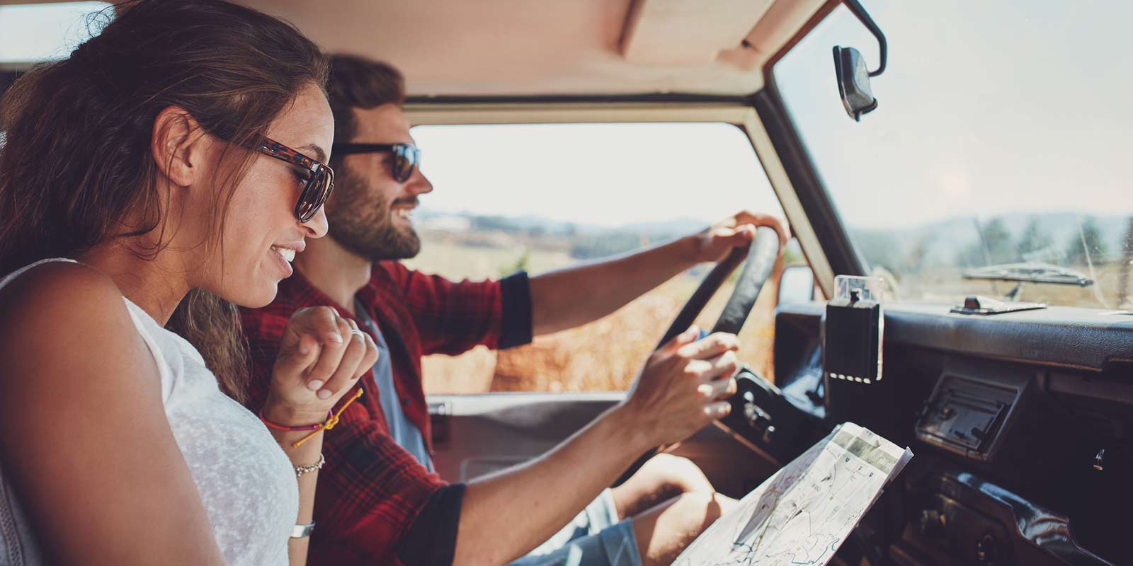 A young couple smile as they drive through the country together with a map in hand.