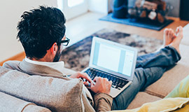 A man sits with a laptop on his lap in his living room .