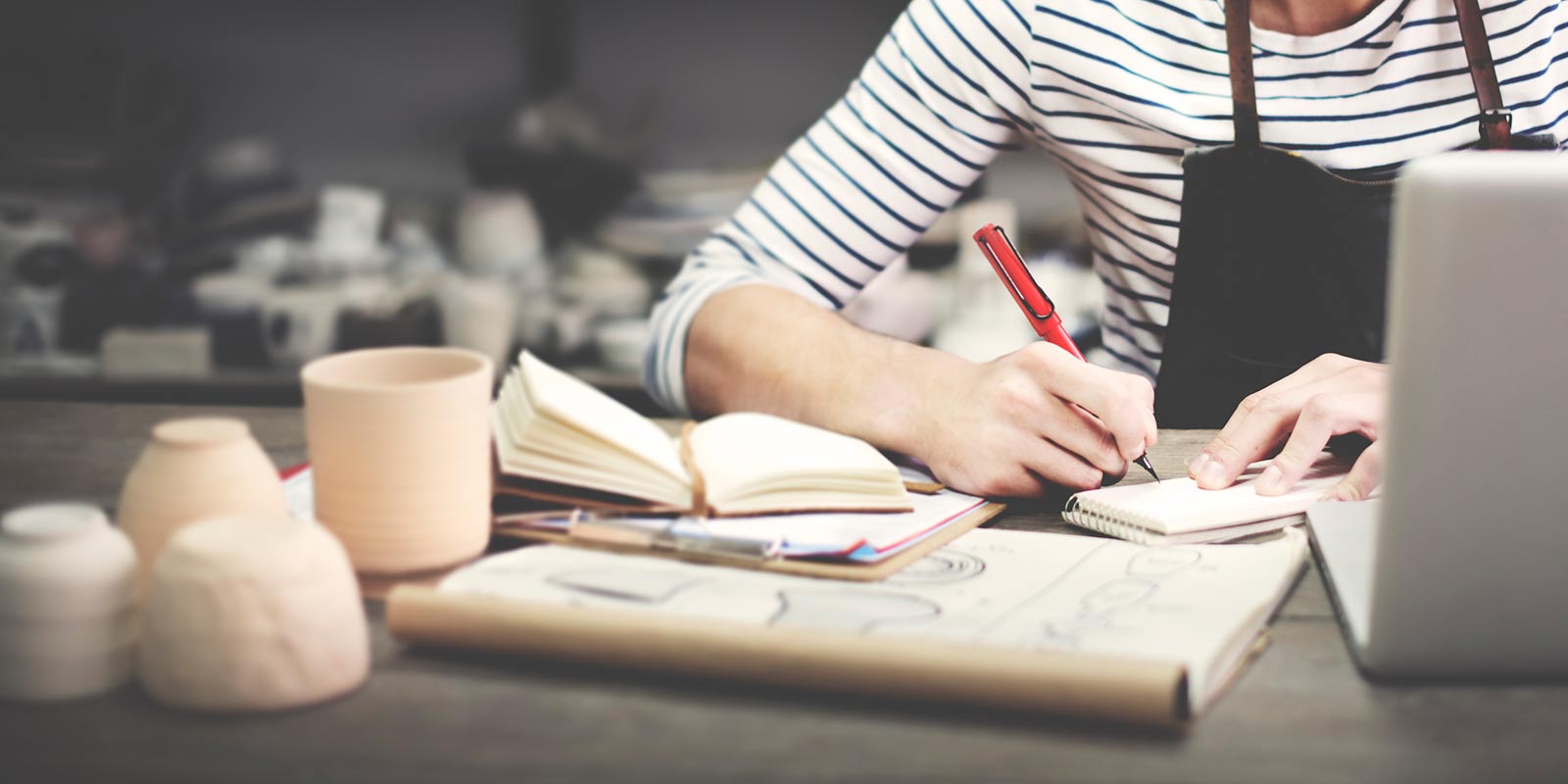 A woman writing on paper as she sits at her desk in her ceramics studio.