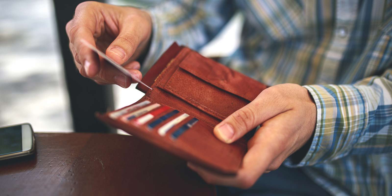 A man pulls a credit or debit card out of his leather wallet.
