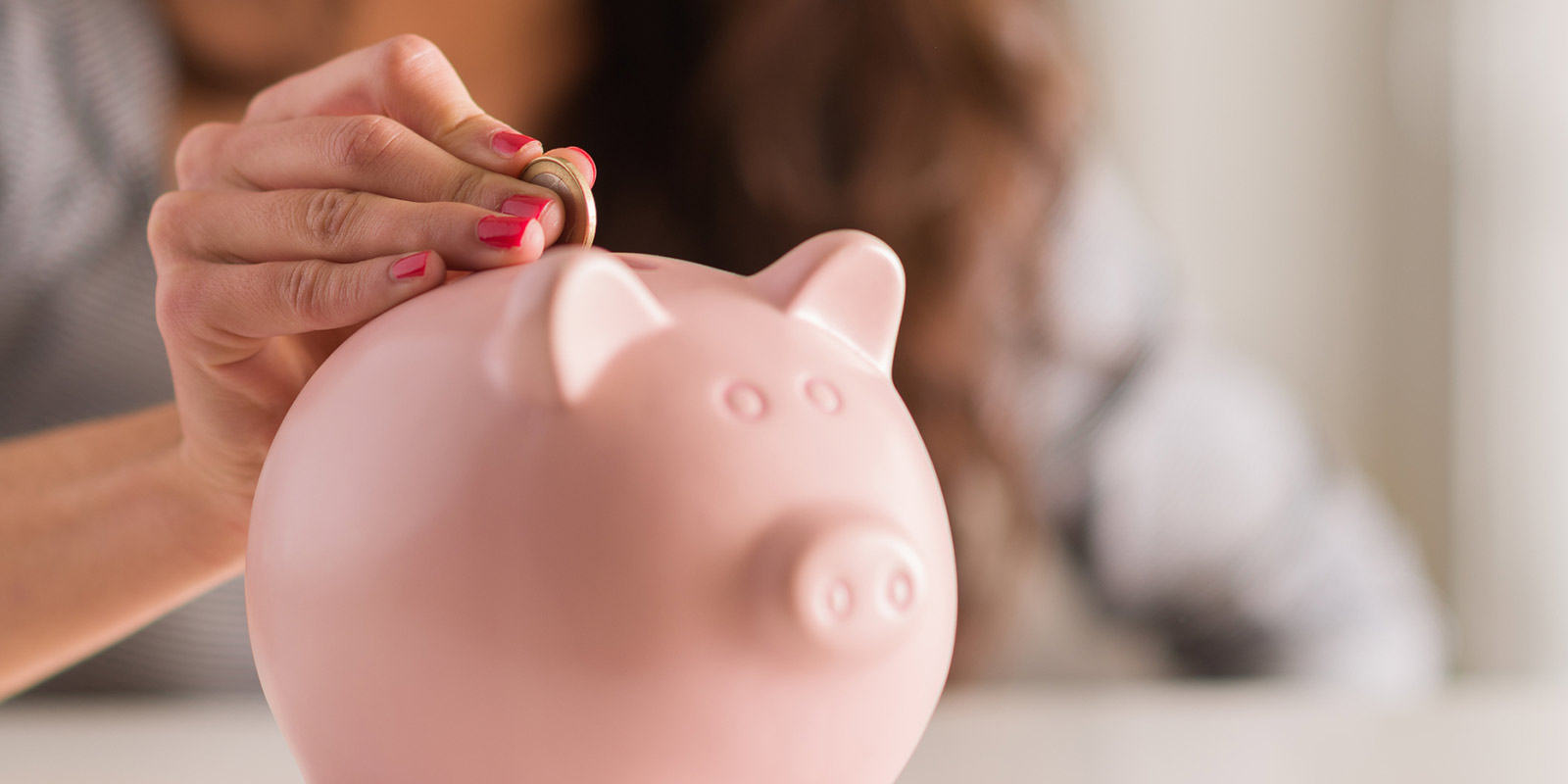 A woman places a coin into a piggy bank.