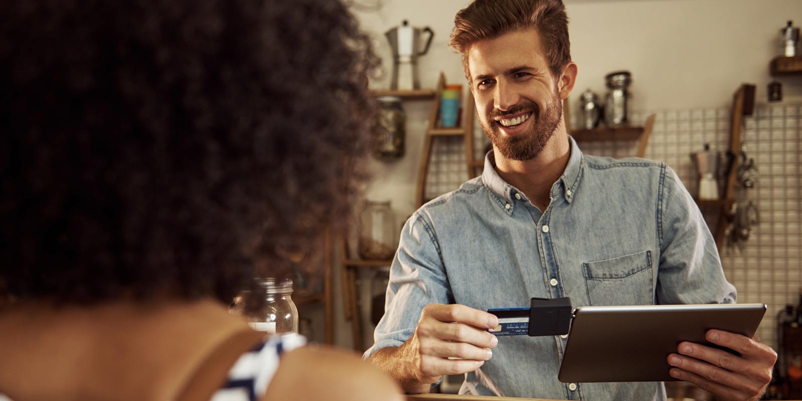 A cashier swipes the credit card of a woman on his tablet.